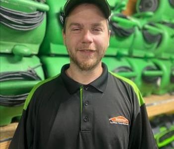Daniel is in a SERVPRO black polo shirt in front of rows of green SERVPRO fans